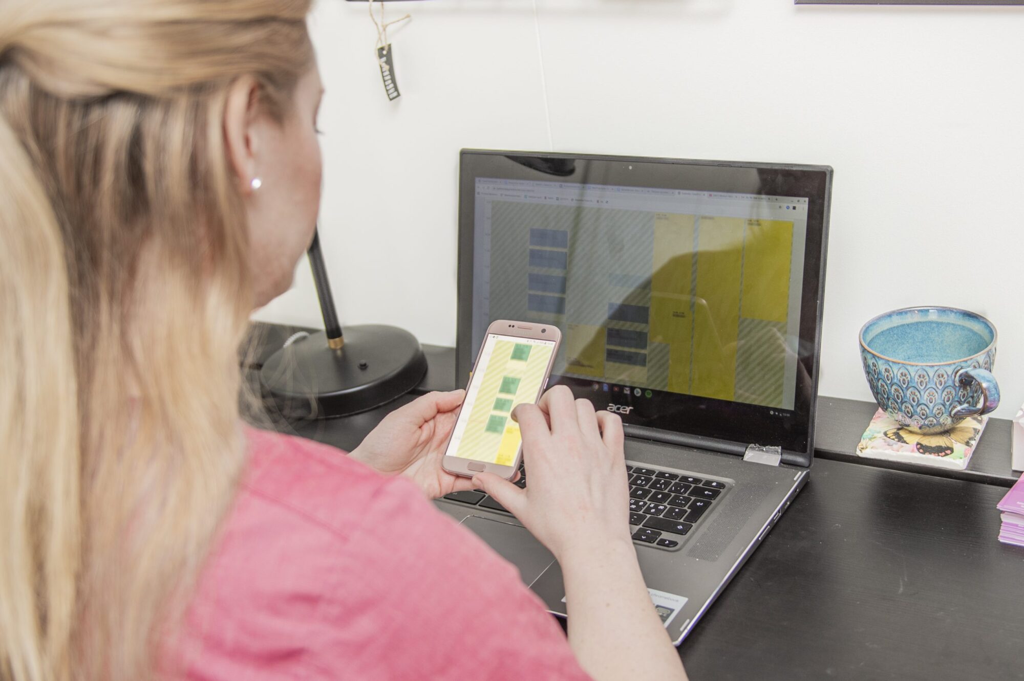 En person ser på deres telefon og har deres kalender på computer åben