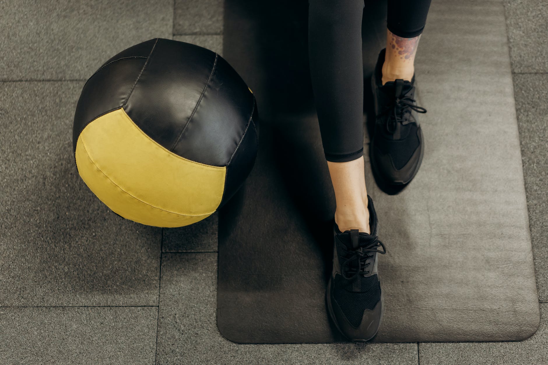 Kvinde der træner med medicinbold på yogamåtte på sort gummigulv