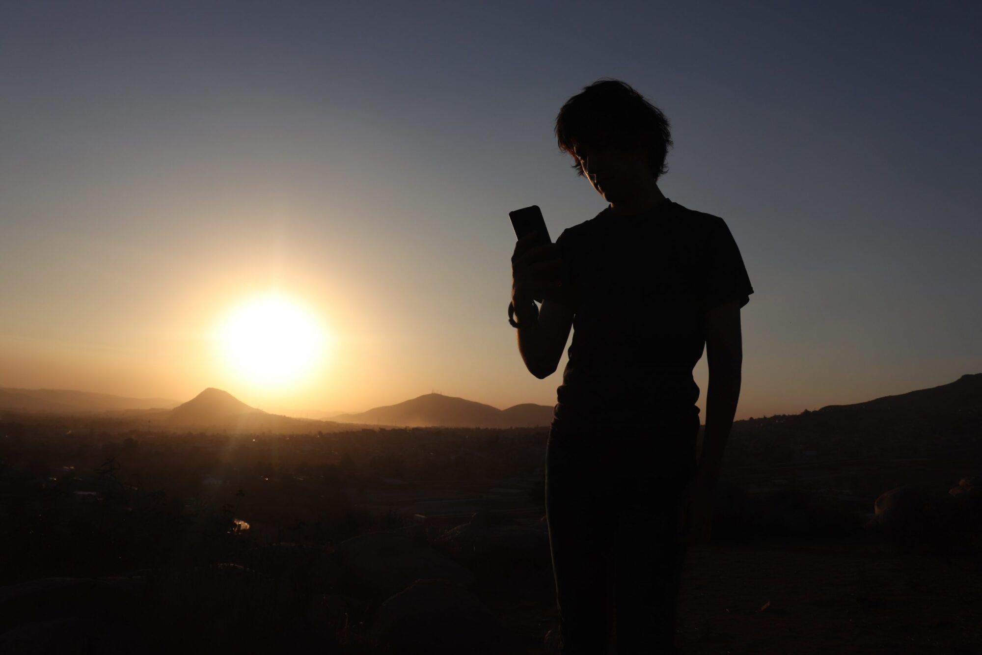 Silhouet af person der kigger på smartphone foran solnedgang