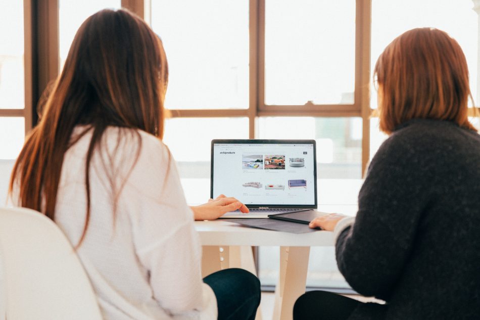 To kvinder der sidder sammen og kigger på en computerskærm ved et skrivebord